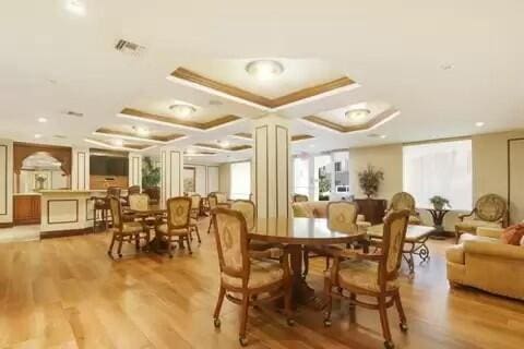 dining space with light wood-style floors, visible vents, and coffered ceiling