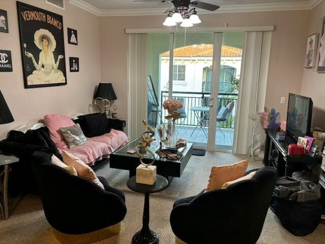 living room featuring a ceiling fan, visible vents, ornamental molding, and carpet flooring