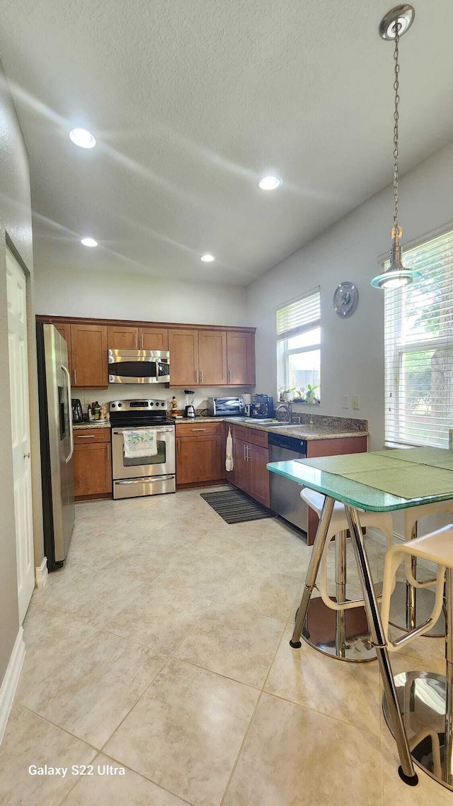 kitchen featuring brown cabinetry, stainless steel appliances, a textured ceiling, pendant lighting, and recessed lighting