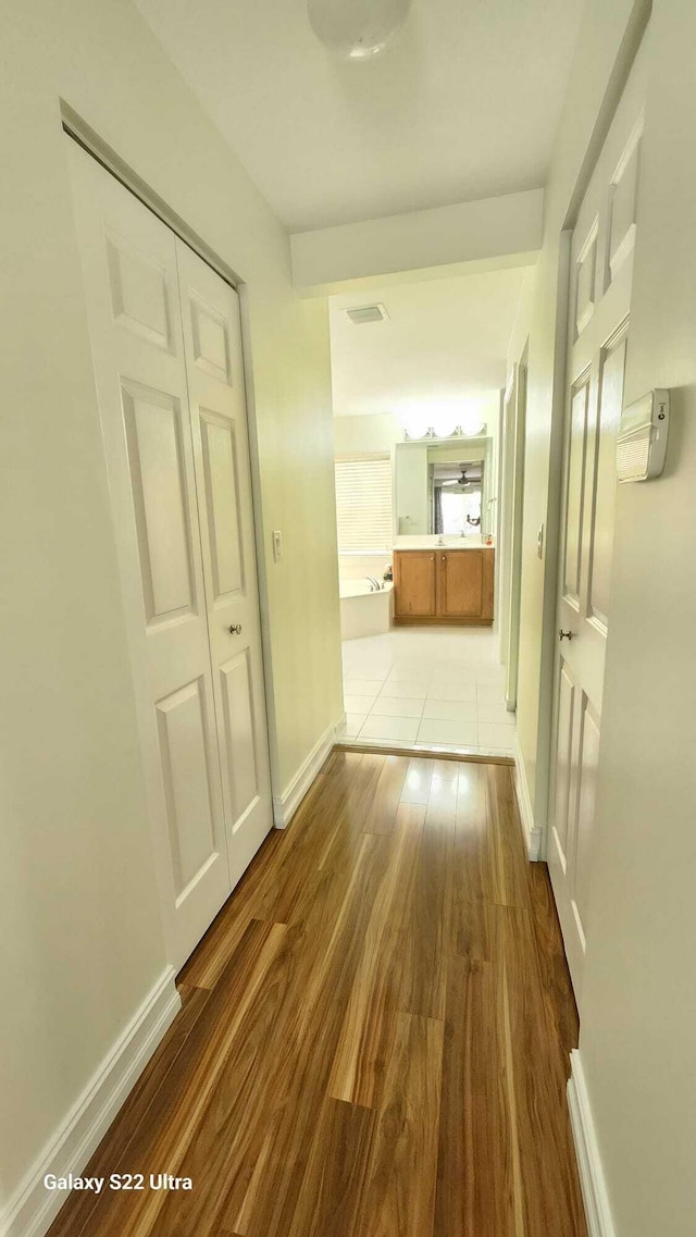 hall featuring light wood-type flooring, visible vents, and baseboards