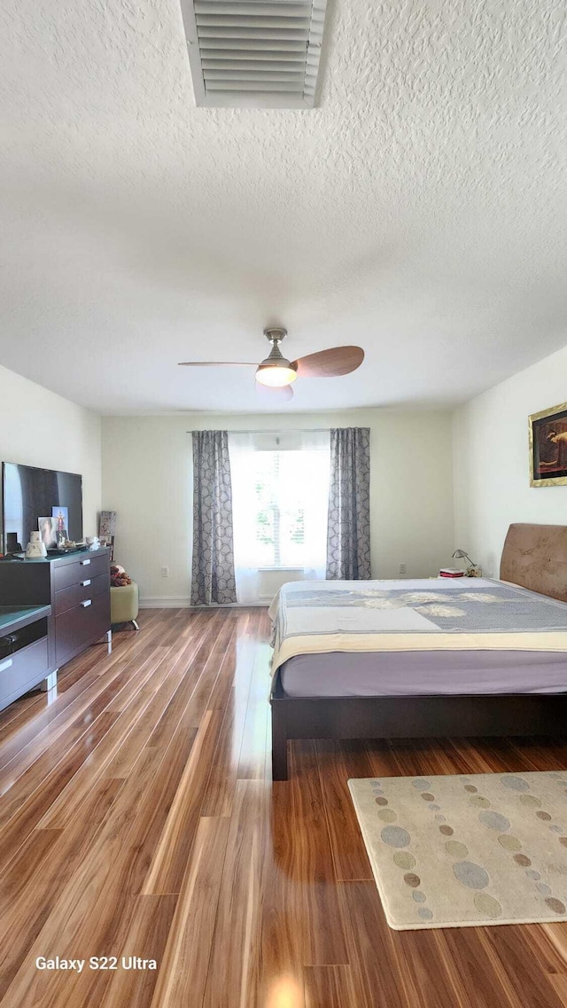 bedroom with visible vents, ceiling fan, a textured ceiling, wood finished floors, and baseboards