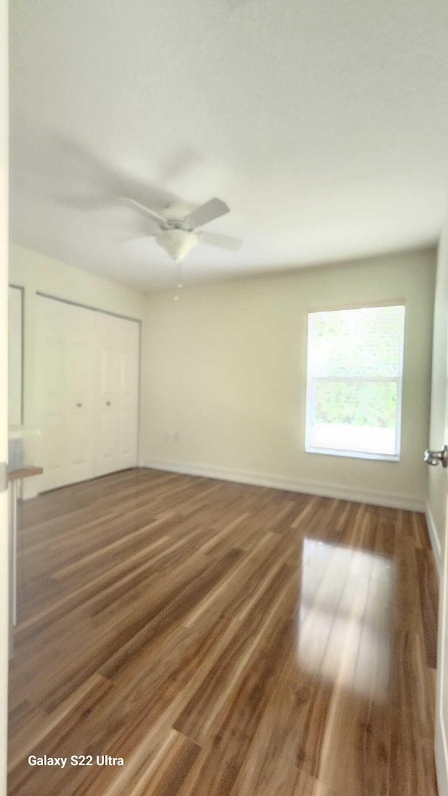 unfurnished bedroom with a ceiling fan, a closet, dark wood finished floors, and baseboards