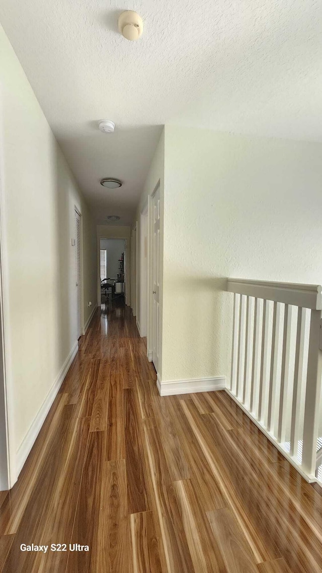 hallway featuring a textured ceiling, dark wood-type flooring, and baseboards