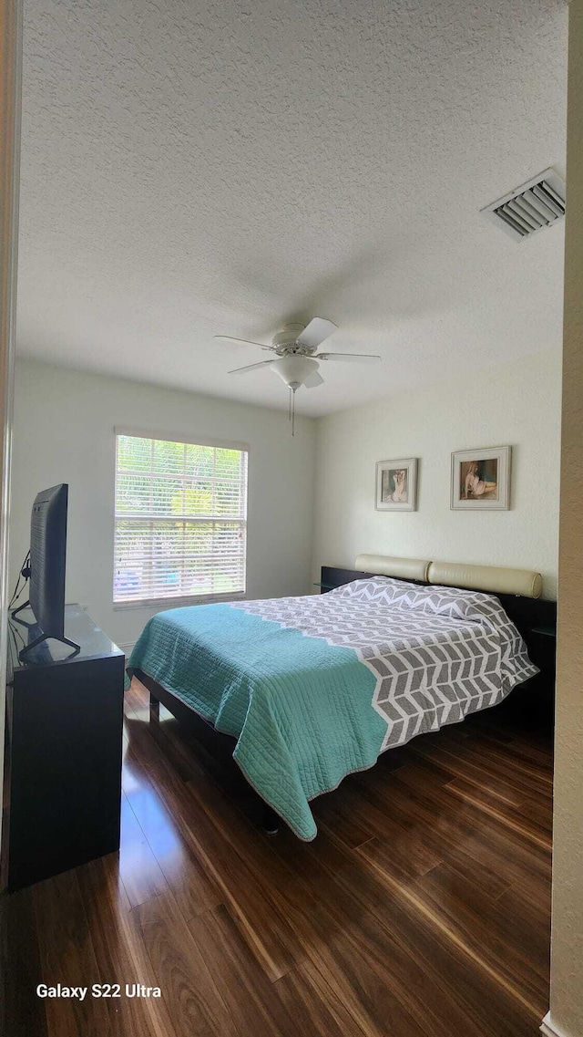 bedroom with dark wood-style floors, visible vents, ceiling fan, and a textured ceiling