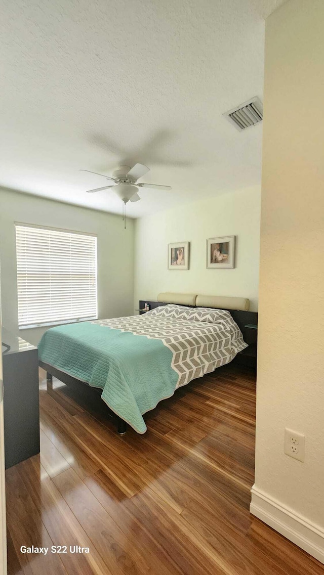 bedroom with a textured ceiling, wood finished floors, visible vents, baseboards, and a ceiling fan