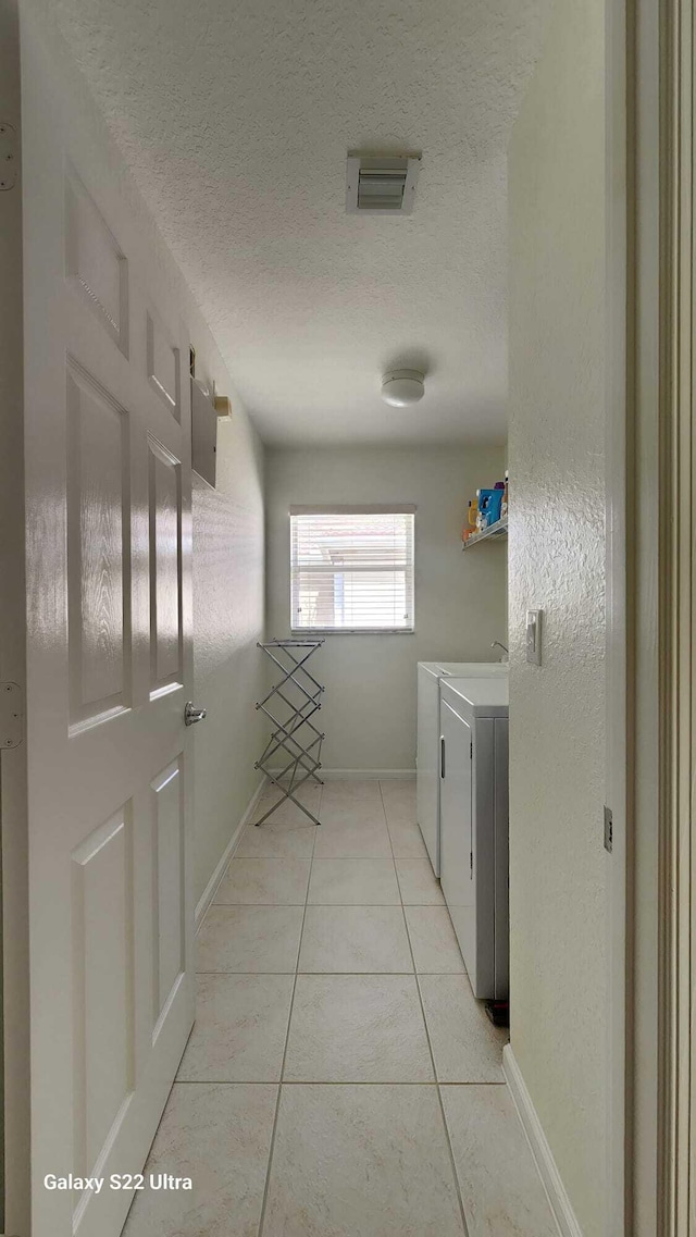 interior space with light tile patterned floors, baseboards, visible vents, a textured ceiling, and separate washer and dryer