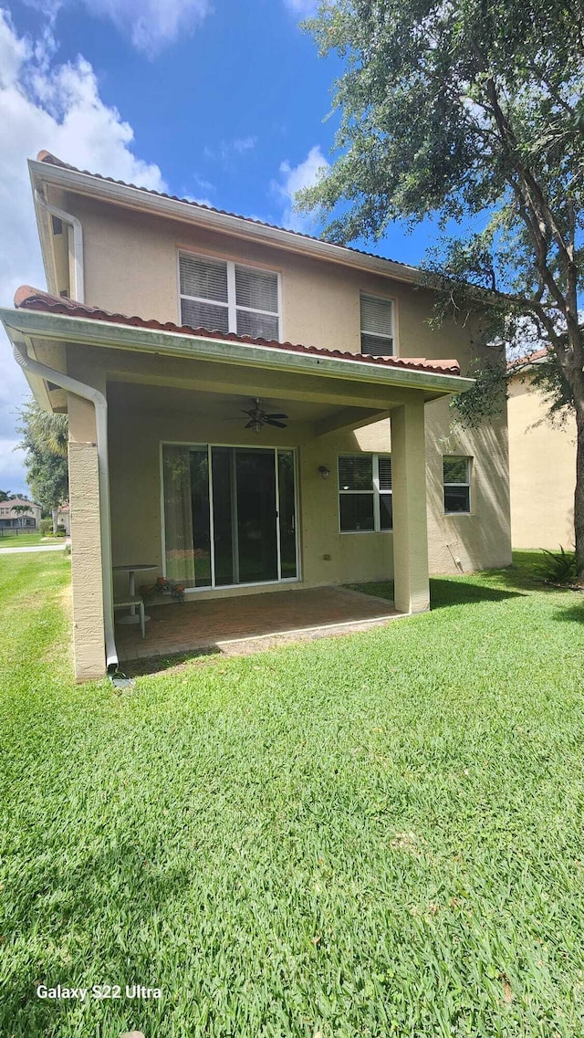 rear view of property featuring stucco siding, ceiling fan, a lawn, and a patio