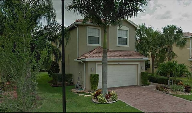 view of front of property with an attached garage, a tiled roof, decorative driveway, stucco siding, and a front yard