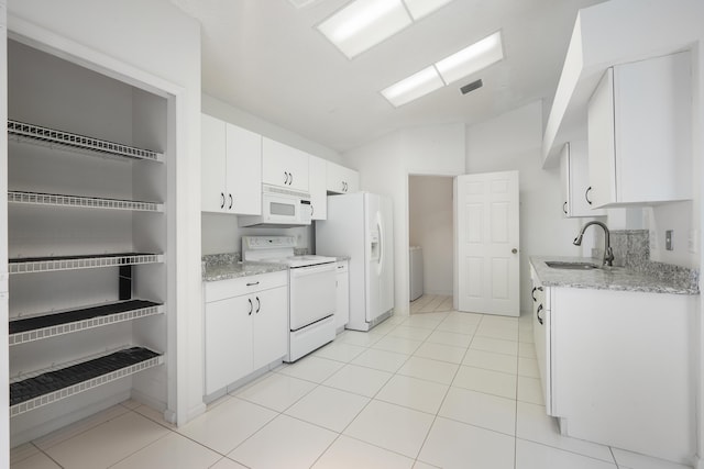 kitchen featuring lofted ceiling, light tile patterned floors, white appliances, a sink, and white cabinetry