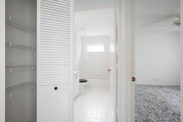 interior space featuring a textured ceiling, tile patterned floors, toilet, and a ceiling fan