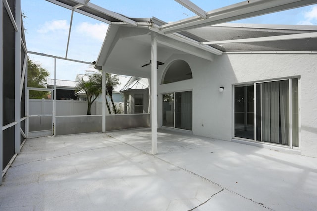 view of patio with ceiling fan, glass enclosure, and fence