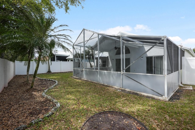 rear view of property featuring glass enclosure, a fenced backyard, a ceiling fan, and a yard