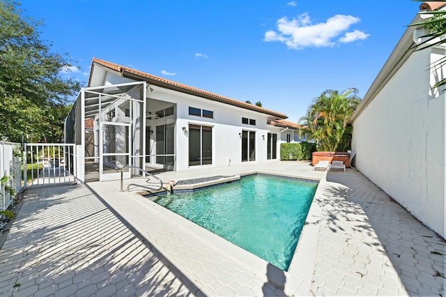 pool featuring glass enclosure, a jacuzzi, fence, and a patio