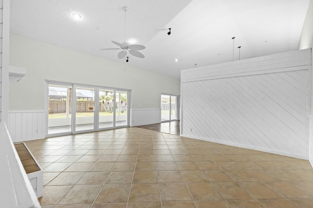 empty room with lofted ceiling, wainscoting, ceiling fan, and light tile patterned floors