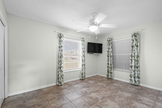 tiled empty room featuring ceiling fan, a textured ceiling, and baseboards