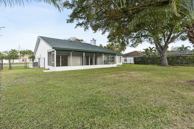 rear view of property featuring a sunroom, a fenced backyard, a chimney, and a lawn