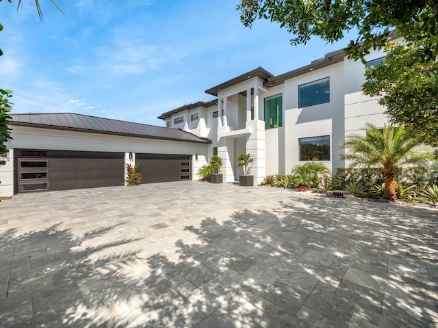 modern home with stucco siding, metal roof, decorative driveway, a garage, and a standing seam roof