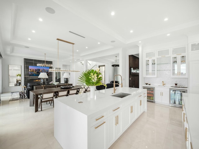 kitchen with beverage cooler, a raised ceiling, a spacious island, and a sink