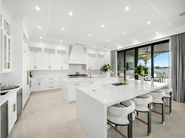 kitchen featuring a sink, wine cooler, light countertops, custom exhaust hood, and a large island with sink