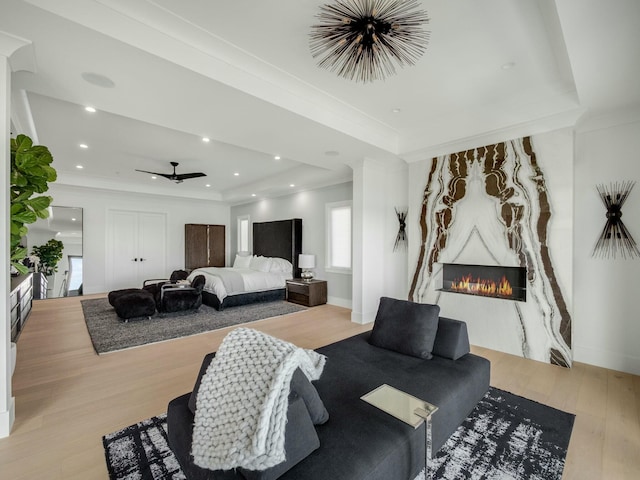 living area with a large fireplace, a raised ceiling, wood finished floors, and ornamental molding