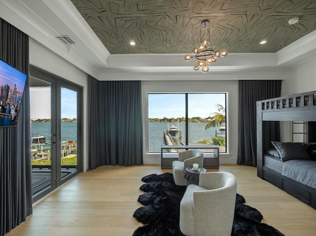 bedroom with access to exterior, visible vents, a tray ceiling, and a water view