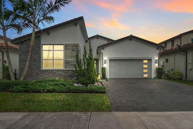 view of front facade featuring a garage, stone siding, decorative driveway, and stucco siding