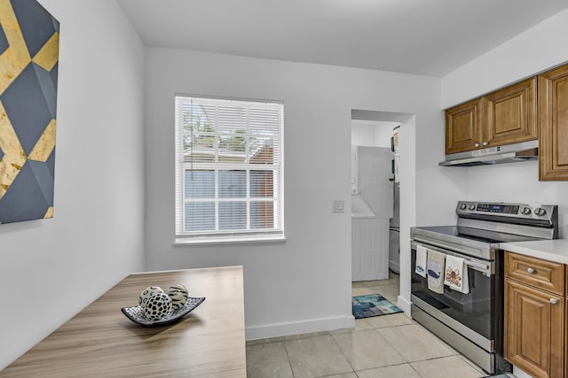 kitchen featuring stainless steel electric range oven, light countertops, brown cabinetry, light tile patterned flooring, and under cabinet range hood