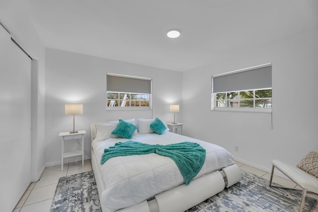 bedroom with multiple windows, light tile patterned flooring, a closet, and baseboards