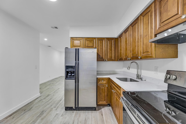 kitchen with stainless steel appliances, light countertops, brown cabinetry, a sink, and under cabinet range hood