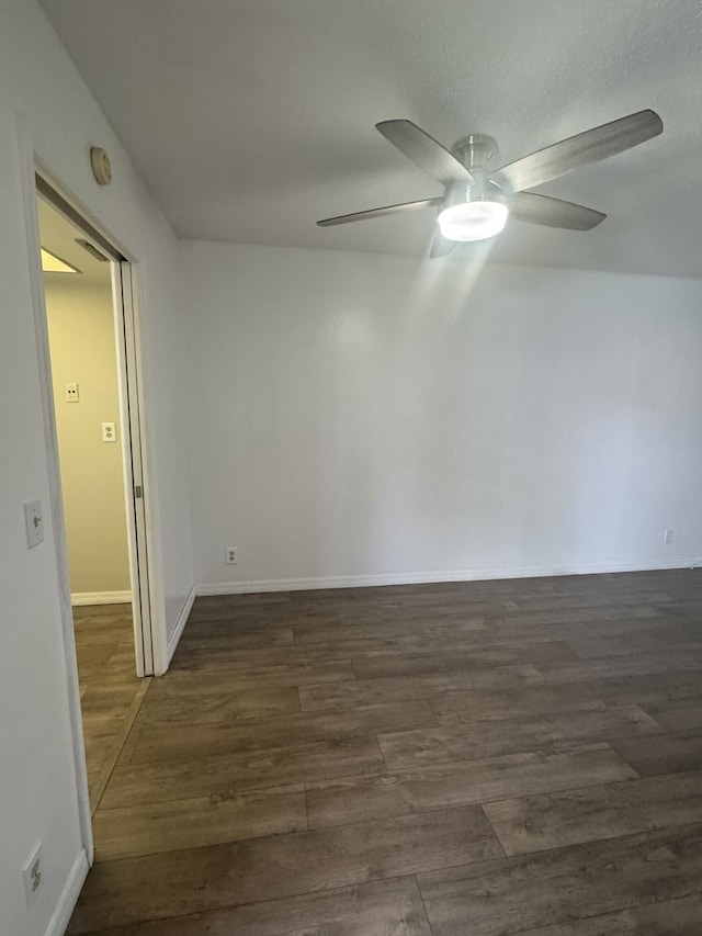 unfurnished room with ceiling fan, baseboards, and dark wood-type flooring