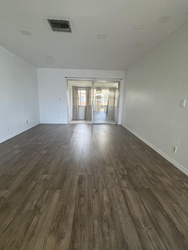 spare room featuring dark wood-style floors, a textured ceiling, visible vents, and baseboards