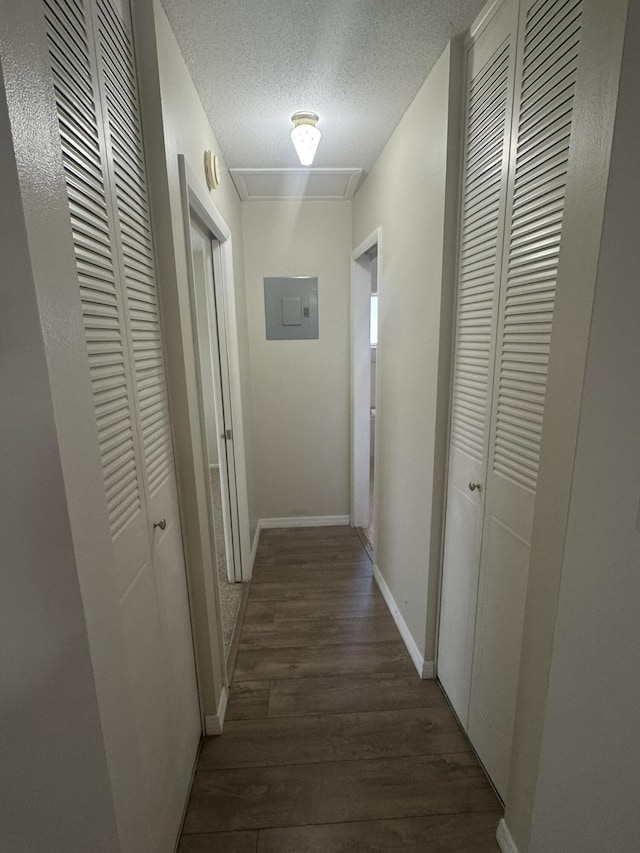 corridor featuring a textured ceiling, dark wood-type flooring, electric panel, and baseboards