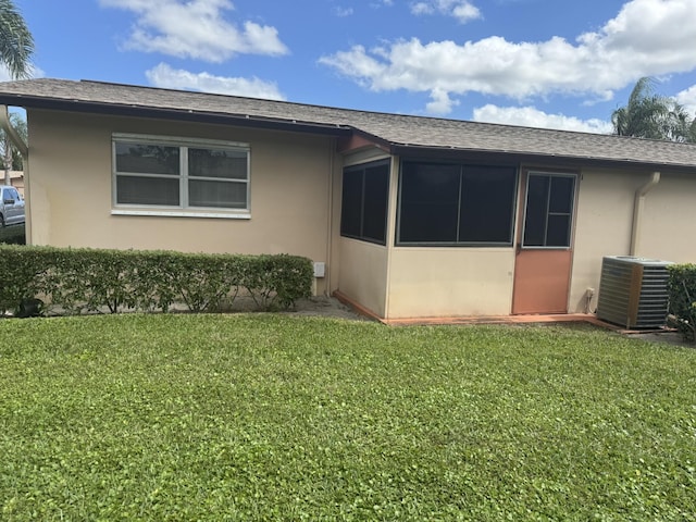 view of side of property featuring a shingled roof, a lawn, central AC, and stucco siding