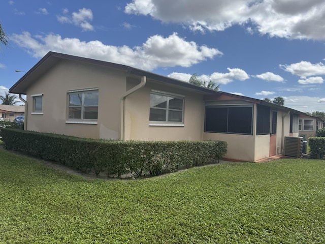 view of side of property featuring central AC unit, a lawn, and stucco siding