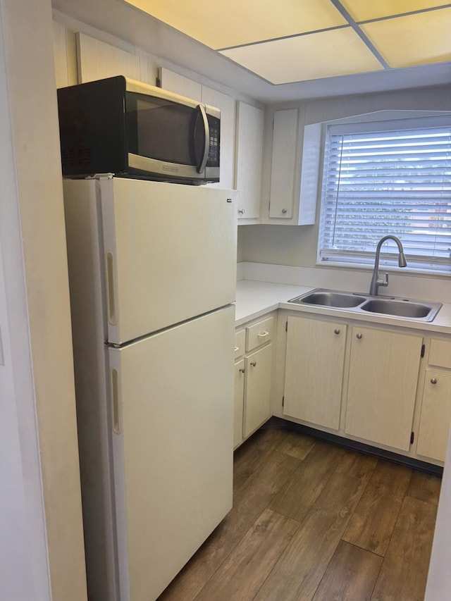 kitchen with a sink, light countertops, freestanding refrigerator, stainless steel microwave, and dark wood finished floors