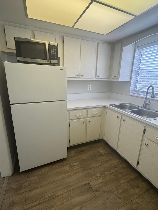 kitchen with dark wood-style flooring, light countertops, stainless steel microwave, freestanding refrigerator, and a sink