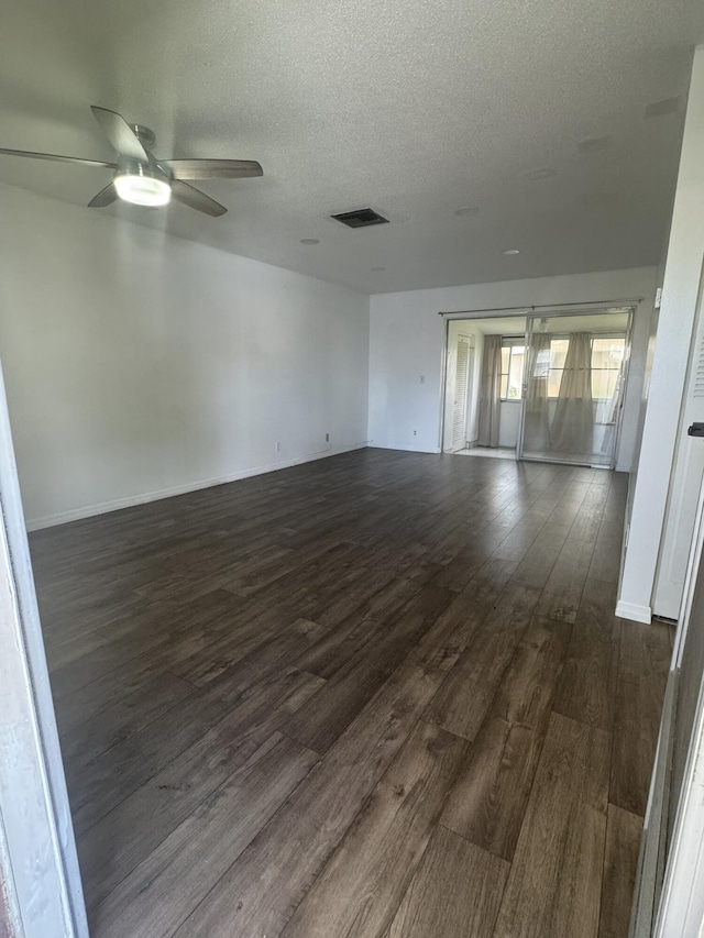 empty room with ceiling fan, visible vents, dark wood finished floors, and a textured ceiling