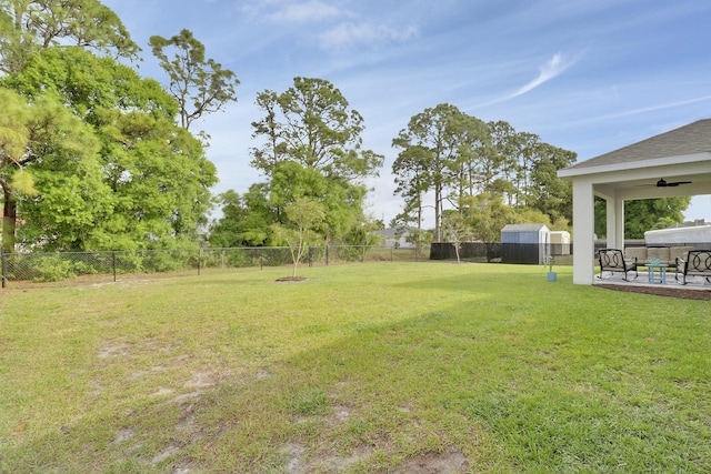 view of yard featuring an outbuilding, a shed, a patio, a fenced backyard, and ceiling fan
