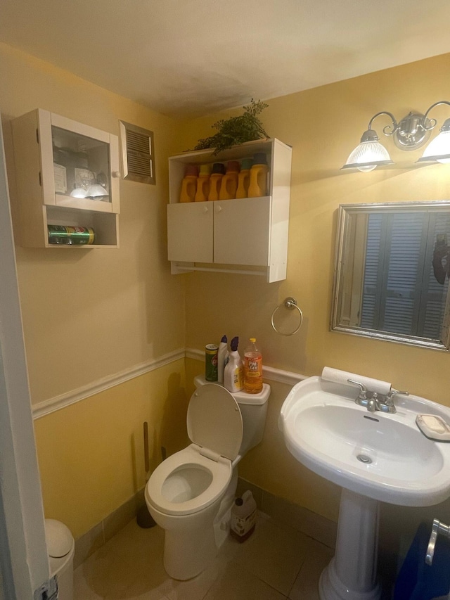 half bathroom featuring toilet, a sink, visible vents, baseboards, and tile patterned floors