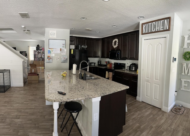 6101 NW Painted Bunting Ct, Port Saint Lucie, FL 34986 - kitchen featuring a sink, black appliances, wood finished floors, a breakfast bar, and light stone countertops