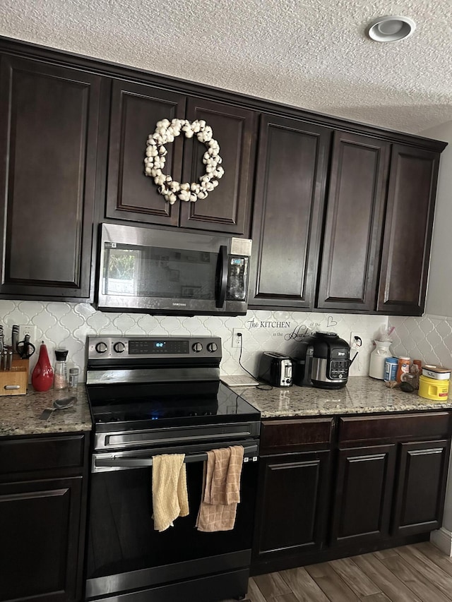 6101 NW Painted Bunting Ct, Port Saint Lucie, FL 34986 - kitchen with range with electric stovetop, stainless steel microwave, a textured ceiling, backsplash, and light stone countertops