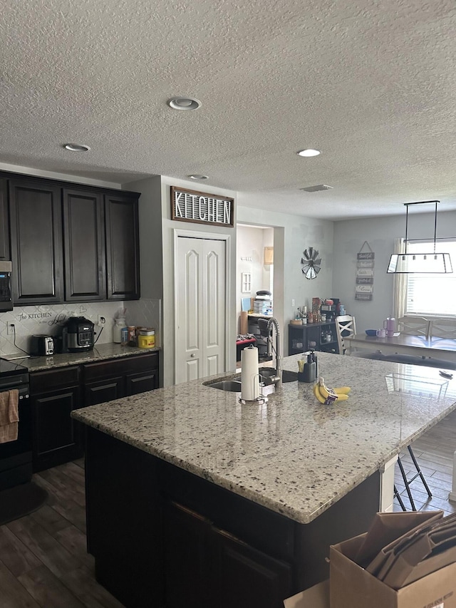 6101 NW Painted Bunting Ct, Port Saint Lucie, FL 34986 - kitchen with a sink, stove, a kitchen island with sink, a textured ceiling, and dark cabinets