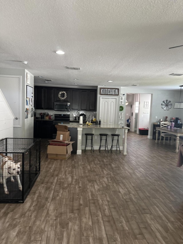 6101 NW Painted Bunting Ct, Port Saint Lucie, FL 34986 - kitchen featuring a breakfast bar, dark cabinets, a textured ceiling, dark wood-type flooring, and a kitchen island with sink