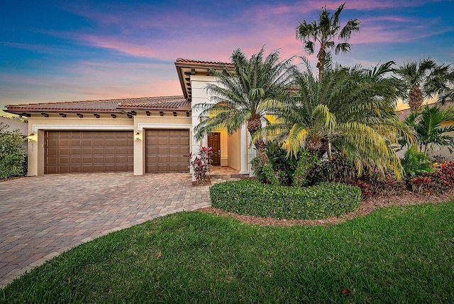 mediterranean / spanish-style home with a tile roof, an attached garage, decorative driveway, a yard, and stucco siding