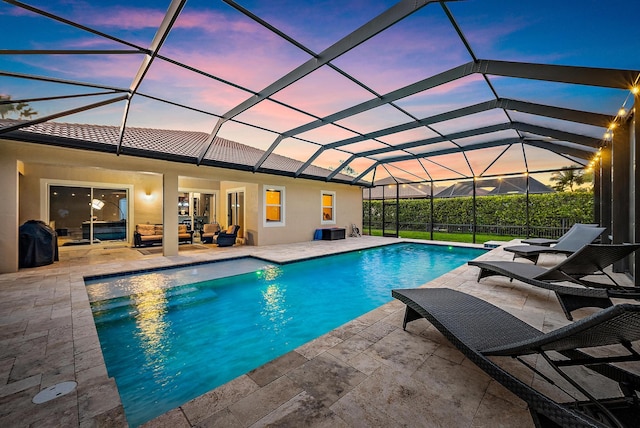 pool at dusk with an outdoor hangout area, a patio, glass enclosure, and an outdoor pool