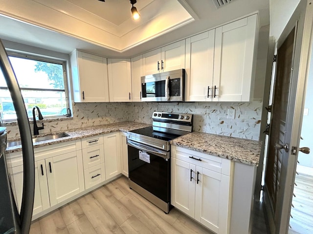 kitchen with light wood finished floors, appliances with stainless steel finishes, white cabinets, and a tray ceiling