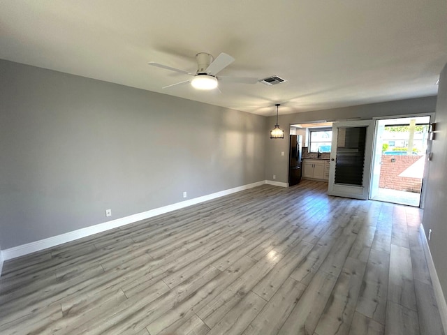 spare room featuring light wood finished floors, baseboards, visible vents, and ceiling fan