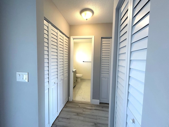 corridor with light wood finished floors, baseboards, and a textured ceiling