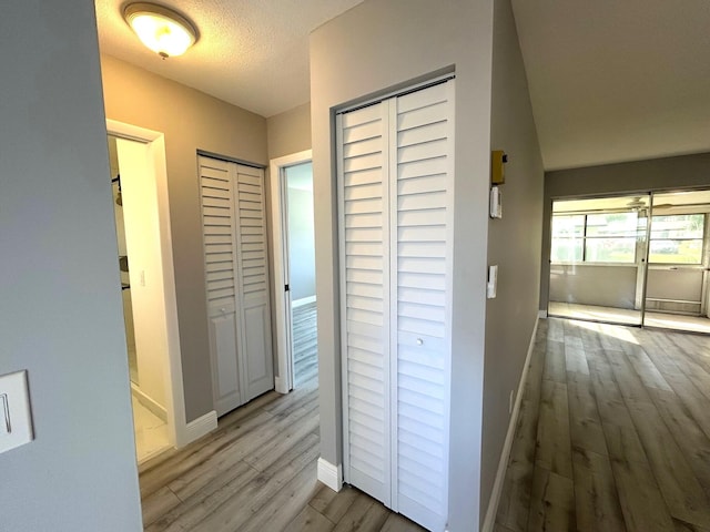 hall featuring a textured ceiling, light wood-type flooring, and baseboards