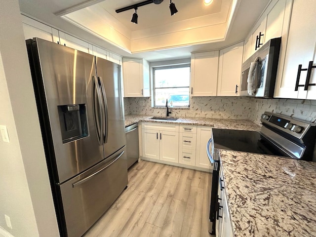 kitchen featuring appliances with stainless steel finishes, a raised ceiling, white cabinetry, and a sink